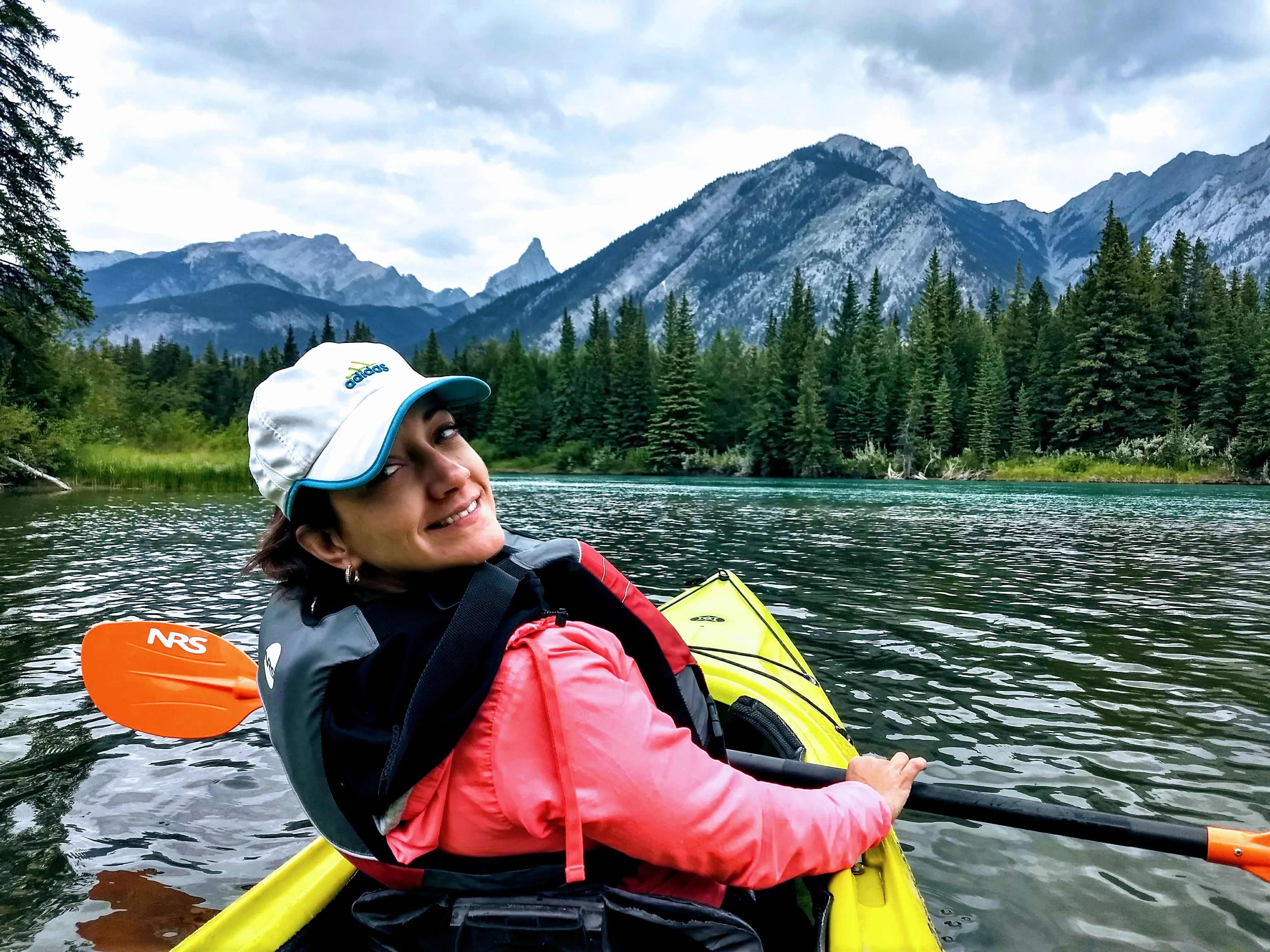 Liz paddling a kayak on a mountain river, looking back over her shoulder.